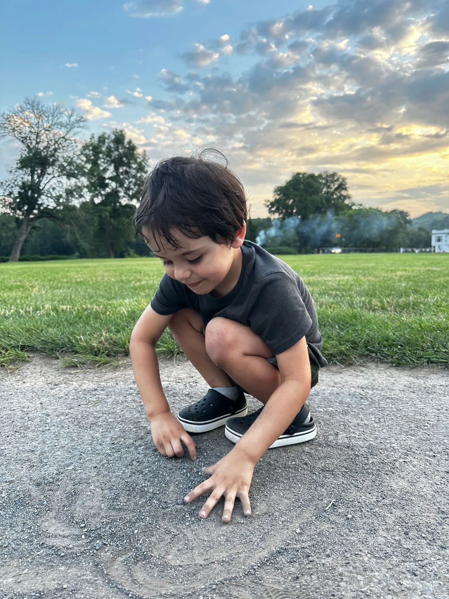 Remy crouched on a path drawing in the sand, with the Shawnee Inn's big green field and a sunset sky behind him